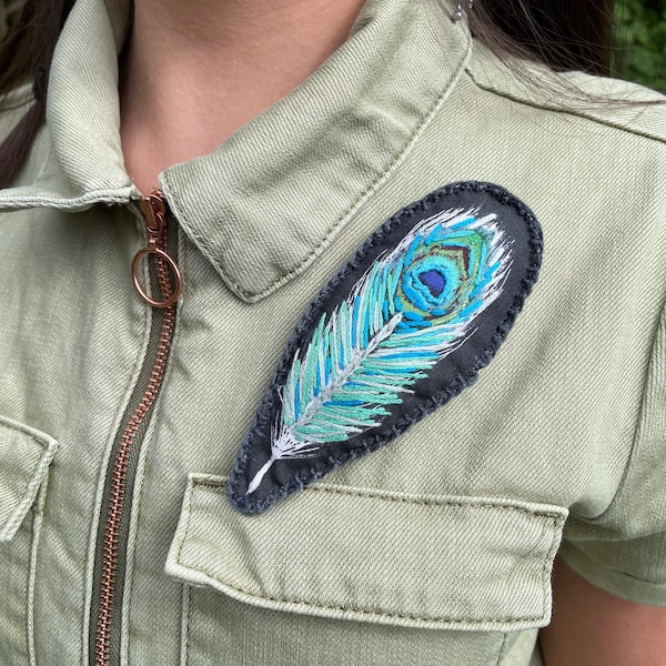 Broche unique en plumes de paon upcyclées brodées à la main sur fond de coton noir, avec support en feutre