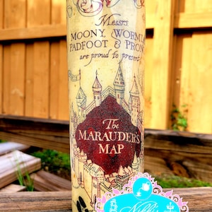 May include: A cylindrical tumbler featuring a design inspired by the Marauder's Map from the Harry Potter series. The tumbler has a cream-colored background with a map design, text, and a burgundy accent. The top rim is glittery.
