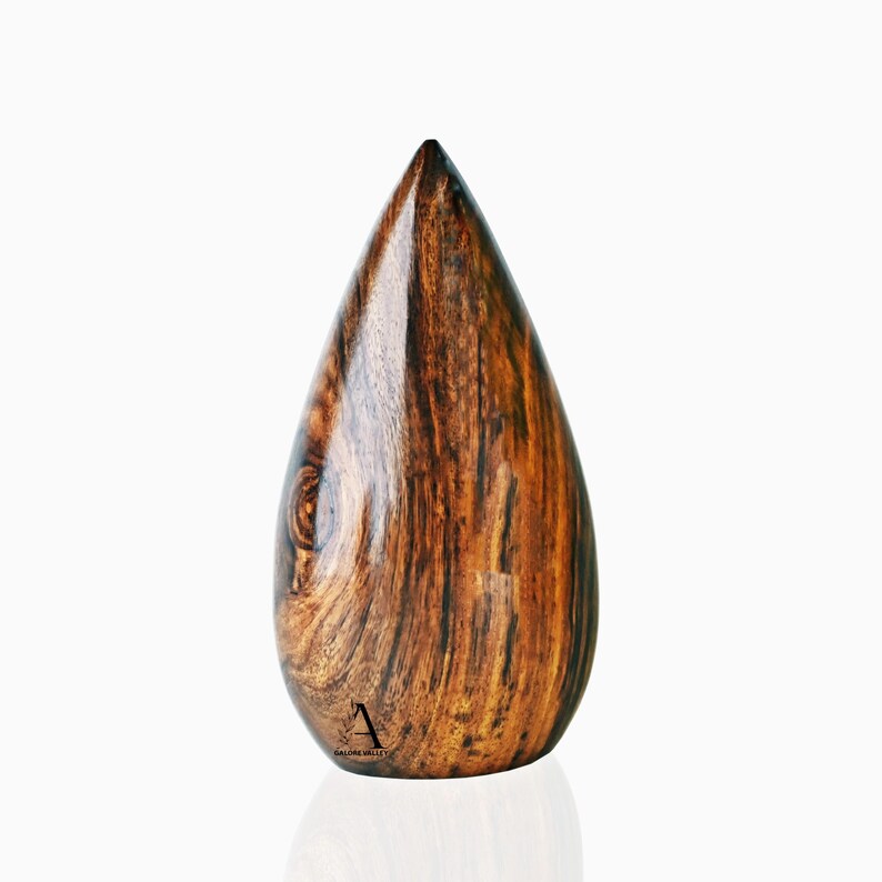 Puede incluir: Una escultura de madera en forma de l&aacute;grima con un patr&oacute;n de veta de madera marr&oacute;n oscuro y marr&oacute;n claro. La escultura est&aacute; pulida y tiene un acabado liso.