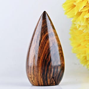 Puede incluir: Un objeto de madera en forma de l&aacute;grima con un patr&oacute;n de veta de madera marr&oacute;n oscuro y negro. El objeto est&aacute; pulido y tiene un acabado liso y brillante.