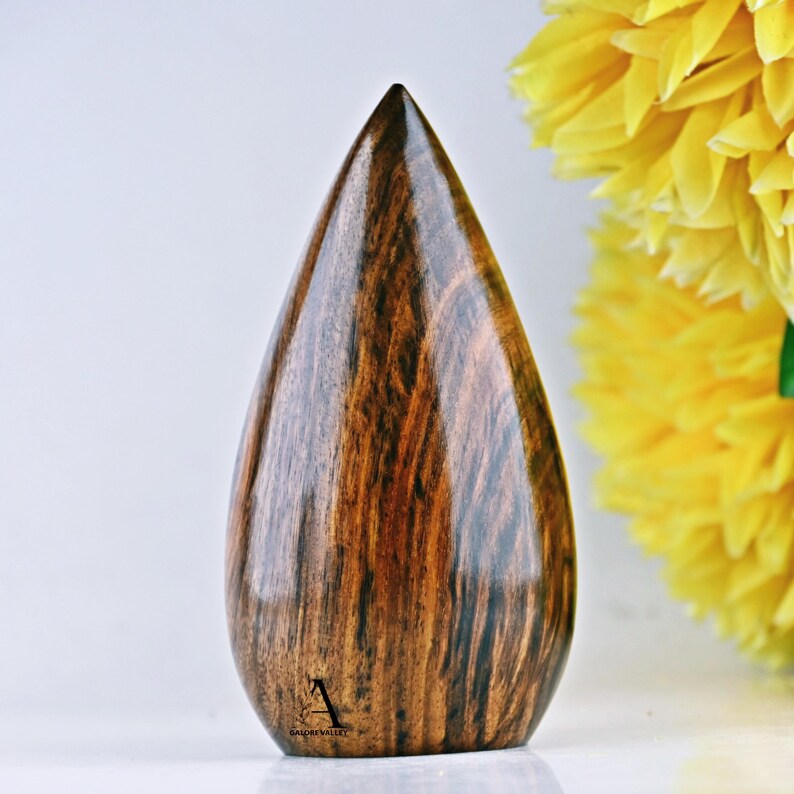 Puede incluir: Un jarr&oacute;n de madera en forma de l&aacute;grima con un patr&oacute;n de veta de madera marr&oacute;n oscuro. El jarr&oacute;n est&aacute; pulido y tiene un acabado liso. La parte inferior del jarr&oacute;n tiene el texto "GALORE VALLEY" en negro.