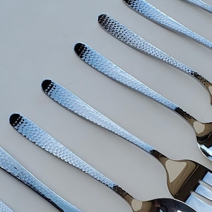 May include: A set of ten silver-toned utensils with hammered textures. The set includes a butter knife, a spoon, a slotted spoon, a fork, and a serving spoon.