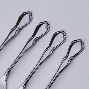 May include: Four silver forks with ornate handles. The forks are arranged in a row, with the handles pointing to the right.