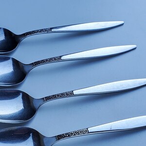 May include: Five silver spoons with ornate designs on the handles. The spoons are arranged in a row, with the handles pointing to the right.