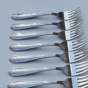 May include: A set of ten silver forks with ornate handles. The forks are arranged in a row, with the tines facing up.