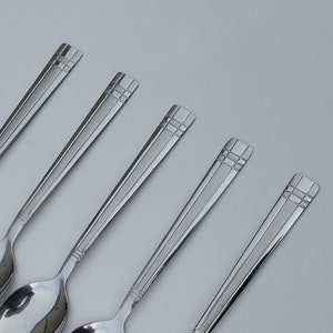 May include: Five silver spoons with a decorative design on the handle. The spoons are arranged in a row, with the handles pointing to the right.