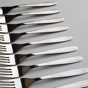 May include: A set of ten silver forks with a patterned design. The forks are arranged in a stack, with the tines of each fork pointing in the same direction.