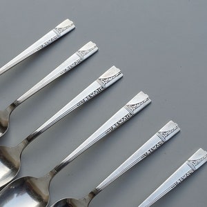 May include: Five silver spoons with ornate handles. The spoons are arranged in a row, with the handles pointing to the right. The spoons are all the same size and shape.