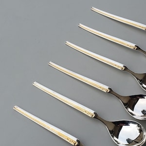 May include: Six silver teaspoons with rounded bowls and ornate handles. The spoons are arranged in a row, with the handles pointing to the right.
