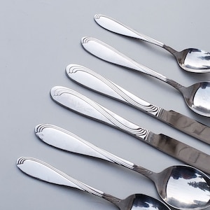 May include: A set of six silver spoons with ornate handles. The spoons are arranged in a fan shape on a white surface.