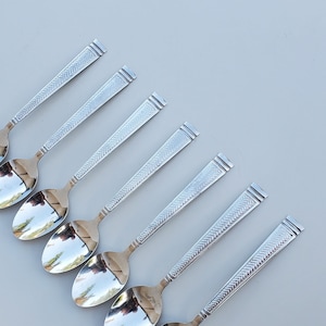 May include: Set of eight silver spoons with an ornate design on the handle. The spoons are arranged in a row, with the handles pointing to the right.