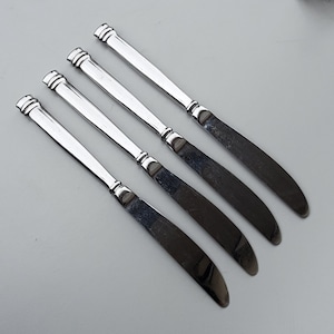 May include: Four silver butter knives with rounded handles.