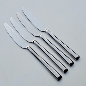 May include: Four silver dinner knives arranged in a row, with the handles pointing to the right.
