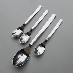 May include: Four silver spoons of varying sizes, arranged in a row on a gray surface.