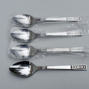 May include: Four silver spoons with decorative handles are packaged in individual plastic sleeves. The spoons are all the same size and shape, and they have a shiny finish.
