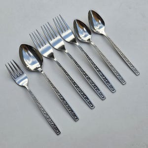 May include: A set of six silver-colored utensils, including three forks and three spoons. The silverware has a floral pattern along the handles. The spoons have a rounded bowl shape, and the forks have four tines.