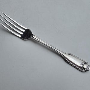 May include: A silver fork with four tines, a decorative handle, and a floral design at the end. The fork is made of a shiny, reflective metal and is set against a gray background. This utensil is suitable for formal dining.