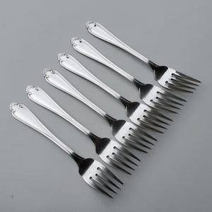 May include: Set of six silver forks with ornate handles. The forks are arranged in a fan shape, with the handles pointing towards the top of the image.