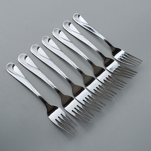 May include: A set of eight silver forks with a decorative, wavy design. The forks are arranged in a row, with the tines pointing towards the right.