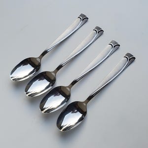 May include: Four silver spoons with a decorative design on the handle. The spoons are arranged in a row, with the handles pointing to the right.