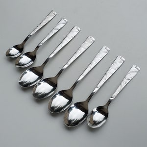 May include: Set of eight silver spoons with an ornate design. The spoons are arranged in a row, with the handles pointing to the right.