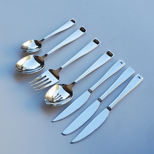 May include: A set of six silver-toned cutlery pieces, including a fork, a spoon, and four knives. The cutlery is arranged in a row on a light blue surface.