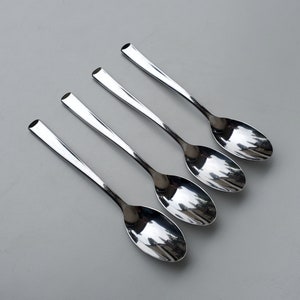 May include: Four silver spoons with rounded bowls and long, slender handles. The spoons are arranged in a row, with the handles pointing to the right.