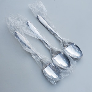 May include: Three silver spoons wrapped in plastic packaging. The spoons have a rounded bowl and a long, slender handle.
