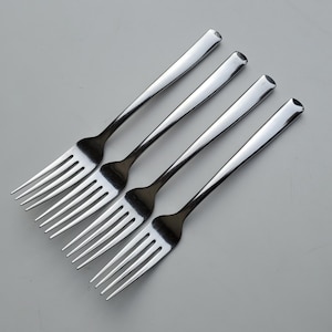 May include: Four silver forks arranged in a fan shape on a white background.