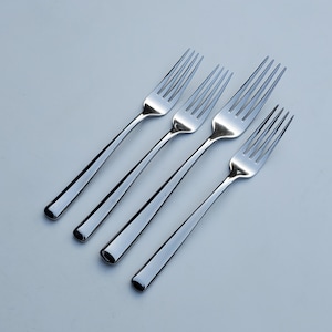 May include: Four silver forks laid out in a row on a white surface.
