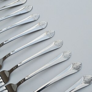 May include: A set of eight silver-plated forks with ornate floral designs on the handles. The forks are arranged in a fan shape on a white surface.