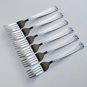 May include: Six silver forks with a decorative swirl design on the handle. The forks are arranged in a row, with the handles pointing to the right.