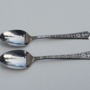 May include: Two silver spoons with ornate floral and fleur-de-lis designs on the handles.