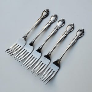 May include: Four silver forks with ornate handles. The forks are arranged in a row, with the handles pointing to the right.