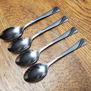 May include: Four silver spoons with a decorative swirl design on the handle. The spoons are arranged in a row, with the handles pointing to the right.
