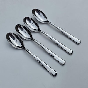 May include: A set of four polished stainless steel spoons arranged in a diagonal row. Each spoon features a smooth, reflective oval bowl and a simple, straight handle with a rounded end, showcasing a clean and uniform metallic finish throughout.