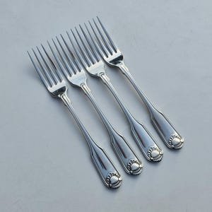 Peut inclure: Quatre fourchettes argentées avec un motif décoratif en forme de coquillage sur le manche. Les fourchettes sont disposées en diagonale sur une surface gris clair, mettant en valeur leur finition polie et leur design élégant.