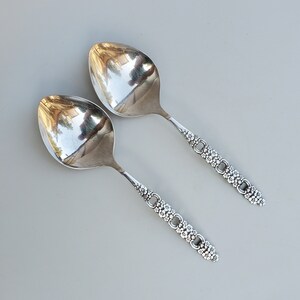 May include: Two silver spoons with ornate floral designs on the handles. The spoons have a rounded bowl shape and are polished to a shine.