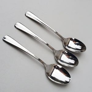 May include: Three silver spoons with shiny, reflective surfaces. The spoons are arranged in a row, with the handles pointing to the right.