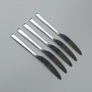 May include: Five silver dinner knives arranged in a row, with the handles pointing to the right and the blades pointing to the left.