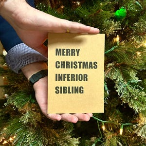 May include: A brown card with the text "Merry Christmas Inferior Sibling" in black lettering.