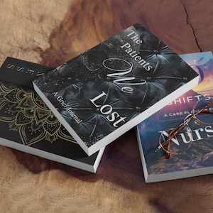 May include: Three books stacked on a wooden surface. The top book is black with white text that reads "The Patients We Lost, A Grief Journal". The middle book is black with a gold mandala design and the text "Journal". The bottom book is blue with white text that reads "Shifts, A Care Plan for Nurses". A pair of round glasses is on top of the bottom book.