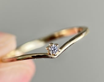 May include: A delicate gold ring with a single, small, clear gemstone set in the centre. The ring is shaped like a V, with the point of the V facing the wearer.