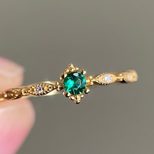 Peut inclure: Une délicate bague en or avec une pierre précieuse verte sertie dans un motif floral. La bande est ornée de petites pierres blanches.