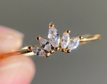 May include: A gold ring with a delicate design featuring multiple small, clear, marquise-shaped stones set in a row.