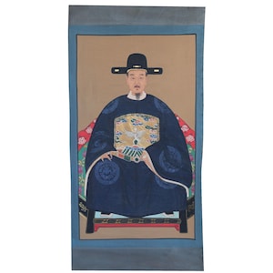 Pode incluir: Retrato de um homem em traje asi&aacute;tico tradicional. Ele usa uma t&uacute;nica azul escura com detalhes ornamentados, um chap&eacute;u preto e est&aacute; sentado em uma cadeira. O fundo &eacute; bege com uma borda azul.