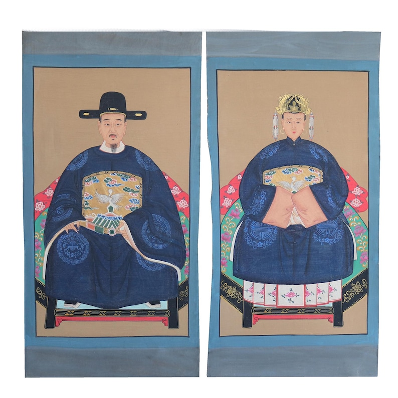 Pode incluir: Dois retratos emoldurados de figuras em trajes asi&aacute;ticos tradicionais. As figuras est&atilde;o sentadas, usando vestes azuis escuras com padr&otilde;es ornamentados e chap&eacute;us. O fundo &eacute; bege com uma borda azul.