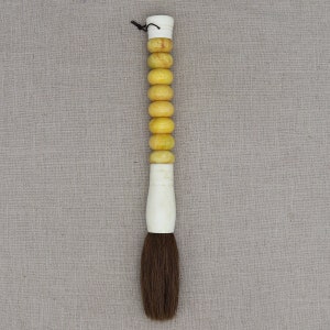 K&ouml;nnte beinhalten: Ein brauner und wei&szlig;er Kalligraphie-Pinsel mit einem Griff aus gelben und wei&szlig;en Perlen.