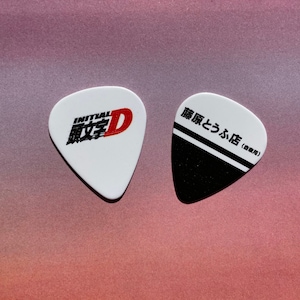 May include: Two guitar picks, one white with the Initial D logo and the text "Initial D" in Japanese, and one black with white stripes and the text "藤原とうふ店 (豆腐屋)"