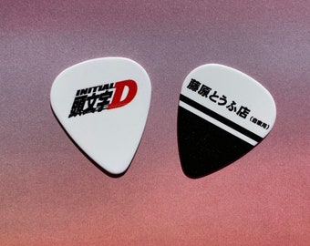 May include: Two guitar picks, one white with the Initial D logo and the text "Initial D" in Japanese, and one black with white stripes and the text "藤原とうふ店 (豆腐屋)"